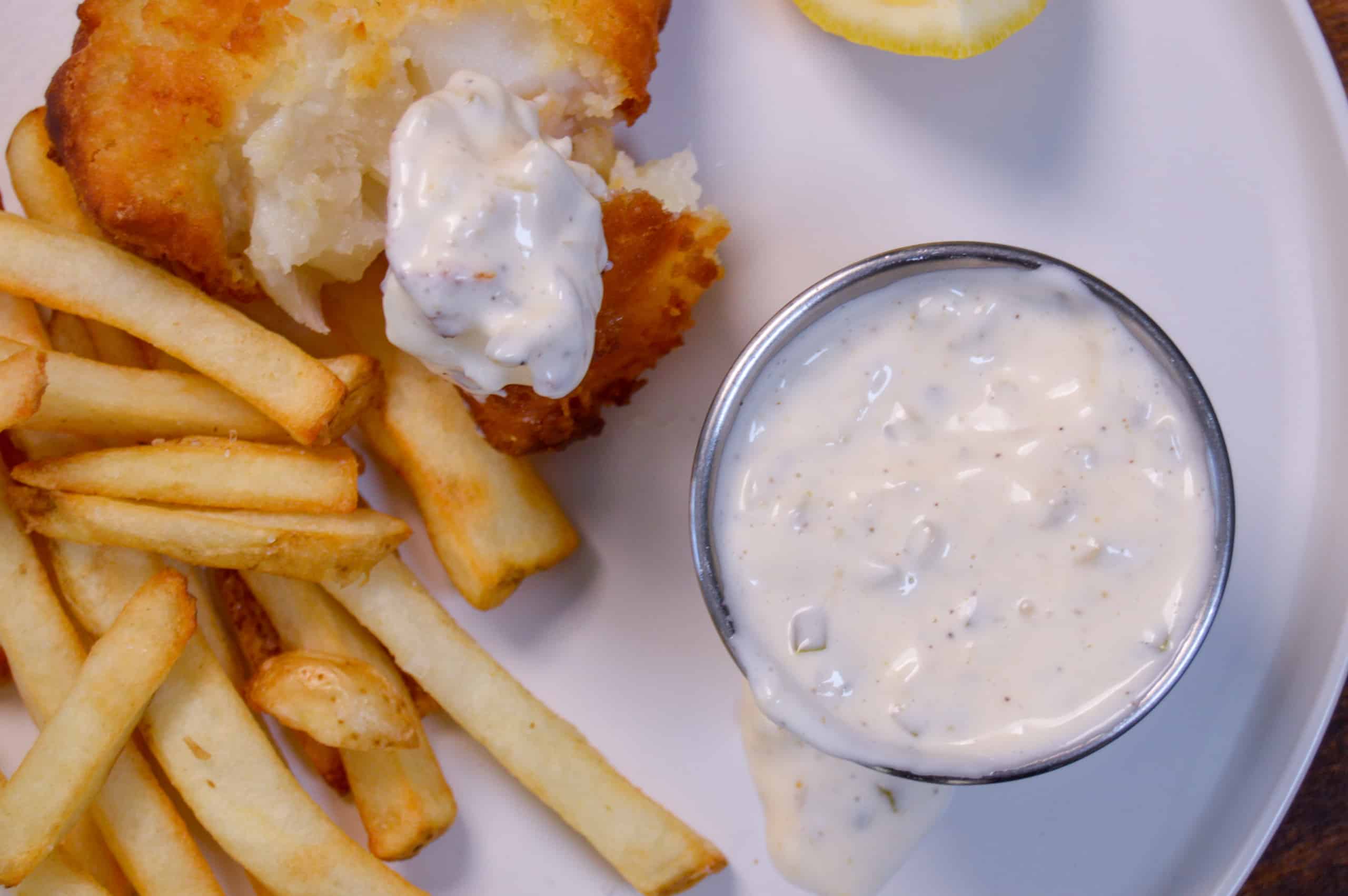 Above shot of tartar sauce with lemon wedge, fish and fries