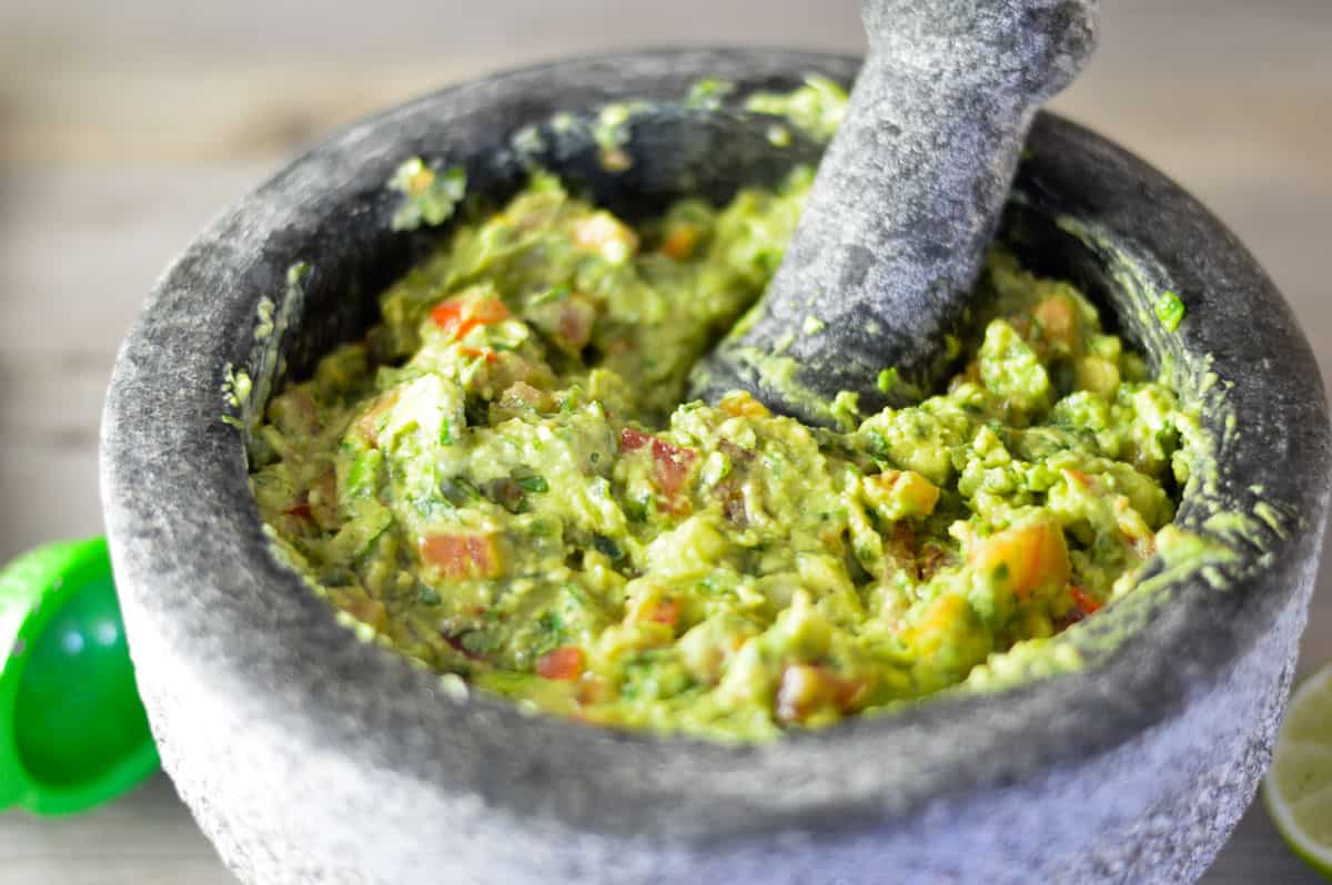 Simple guacamole in Mexican stone bowl with pestle and lime juicer
