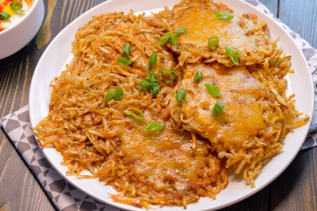 White Plate full of Panini Press Hash Browns, some with melted cheese and green onions atop