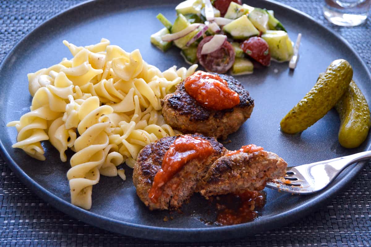 Kotlety Meat patties with spicy ketchup, noodles, salad and pickles