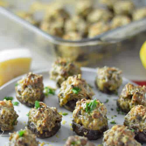 Italian Sausage Stuffed Mushrooms on white plate with parmesan cheese block and more in glass pyrex dish in background.