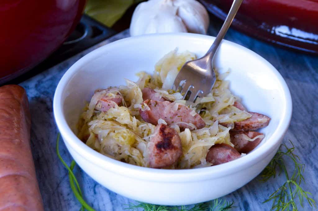 Bigos in a white bowl with fork and Polish sausage
