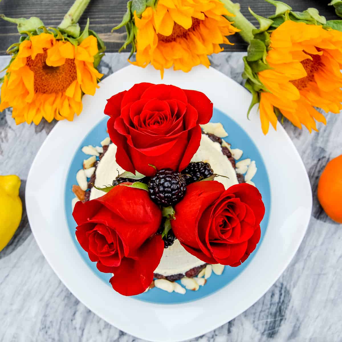 Pascha Crustless Cheesecake with floral, berry decorations and sunflowers below