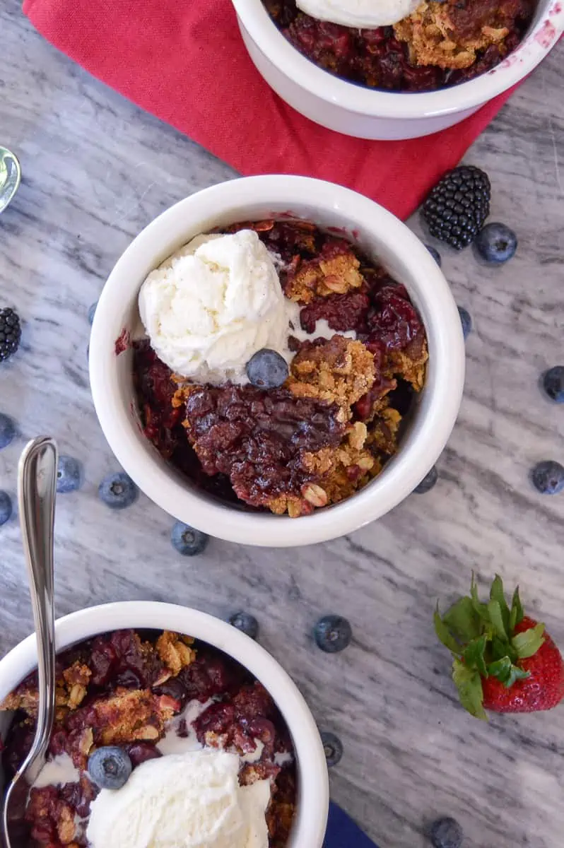 Berry Crisp with vanilla ice cream on top close up with a spoon in one bowl and some fresh berries