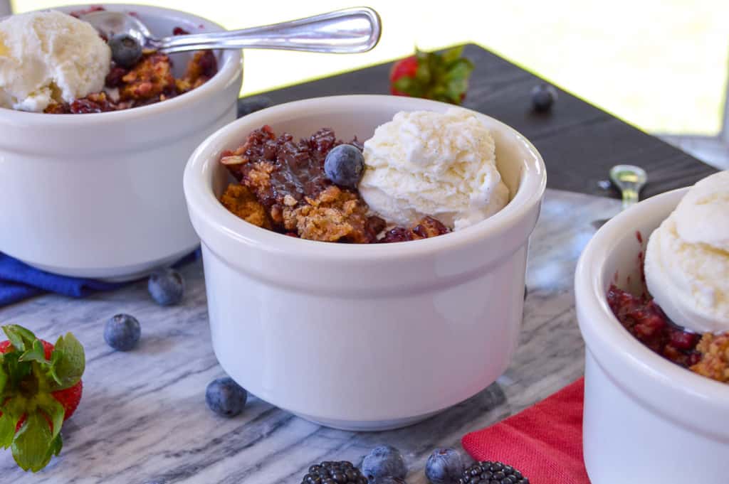 3 bowls of Berry Crisp close up with ice cream and some fresh berries