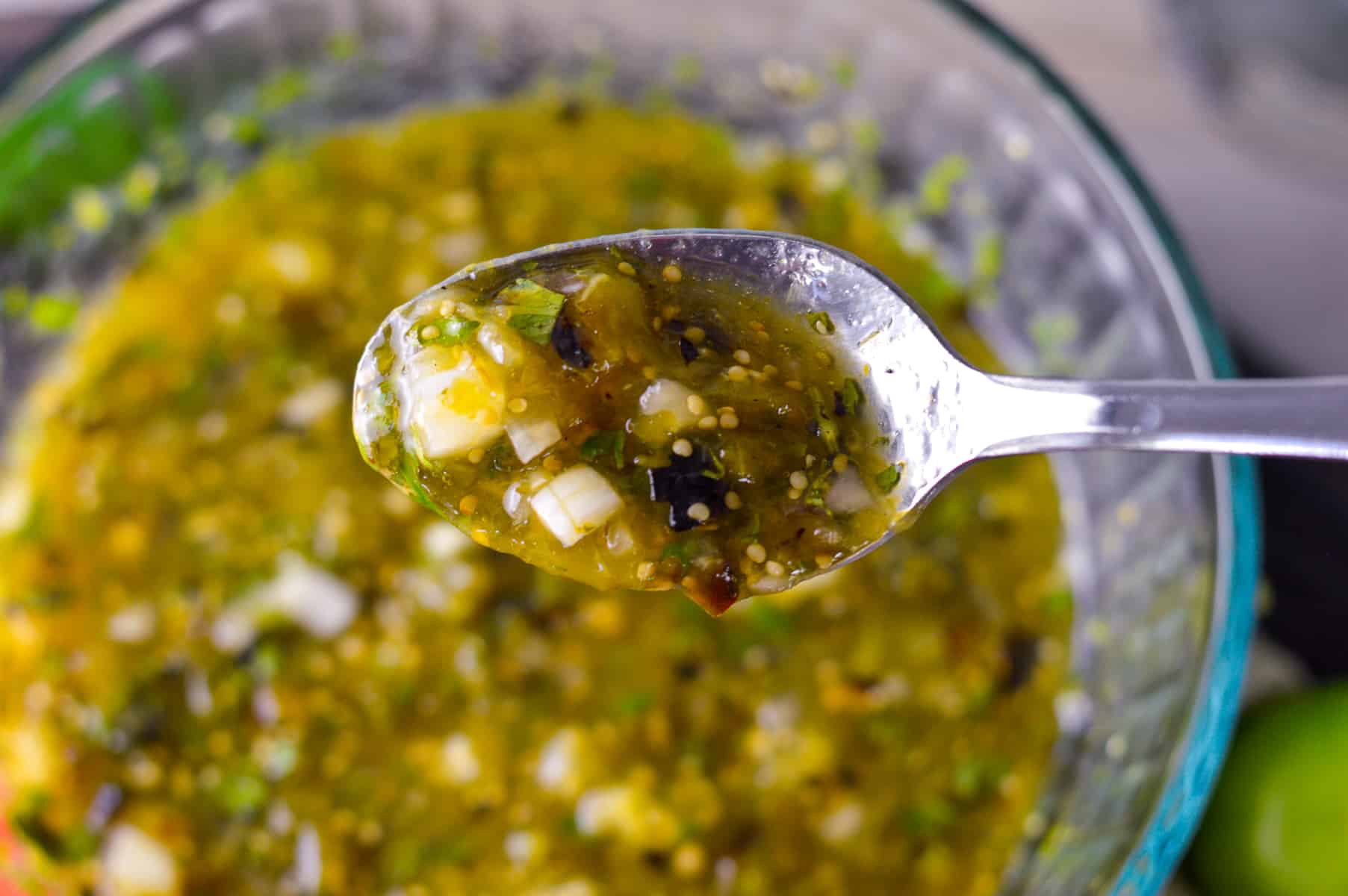 Close up view of salsa verde on silver spoon with glass bowl of salsa verde in background 