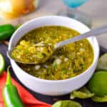 Spicy Salsa Verde in a white bowl with spoon, jalapeno, lime and tomatillos in background