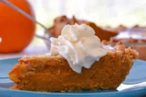 Simple Rustic Pumpkin Pie slice close up on blue plate with whipped cream and pumpkin and another pie in background