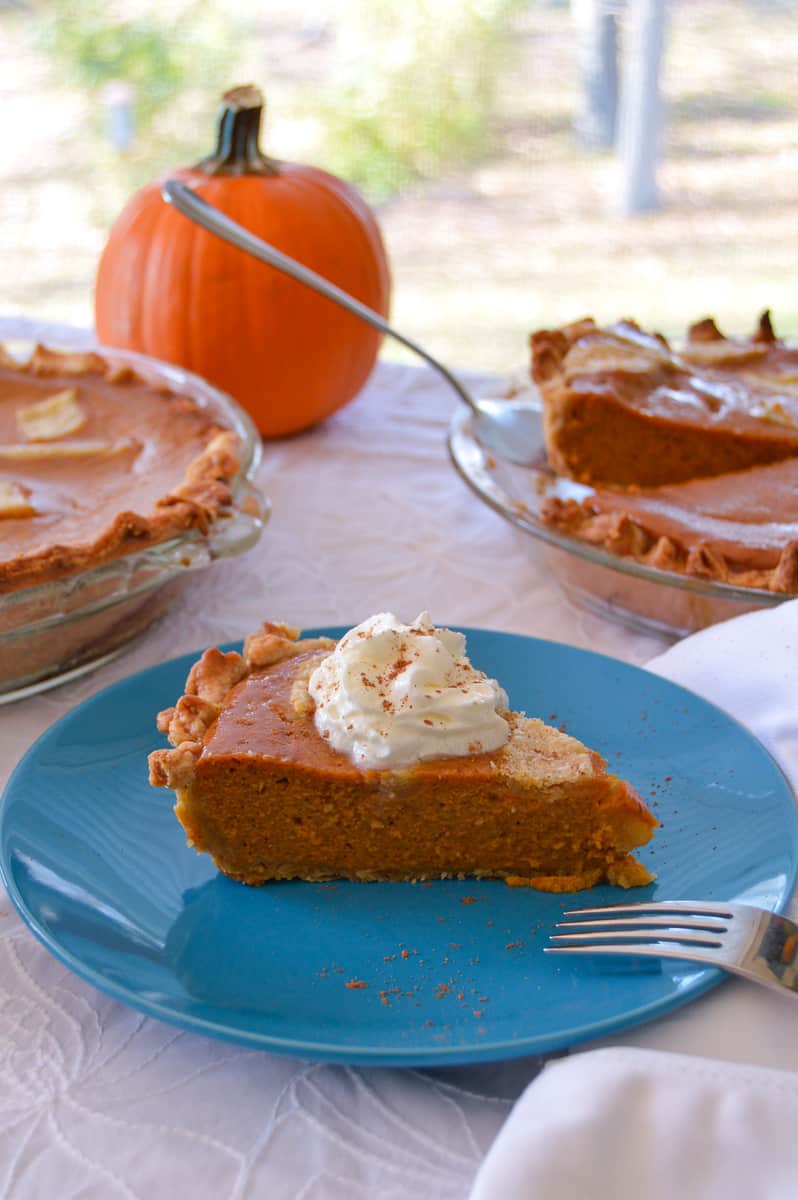 simple pumpkin pie on blue plate with fork and other pies on side next to pumpkin