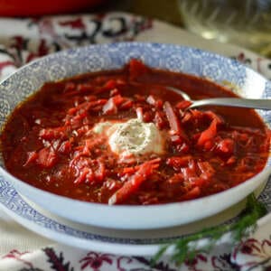 Up close bowl of Borscht with sourcream and dill, carrots and dutch oven