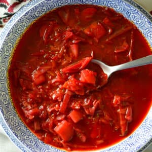 red vegetarian vegan borscht with spoon in blue white bowl on Slavic red white and black napkin