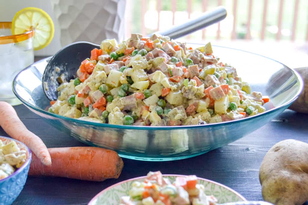  Olivier Russian Potato Salad aka Salat Olivye in a large serving bowl with carrots, potato and water glass around it