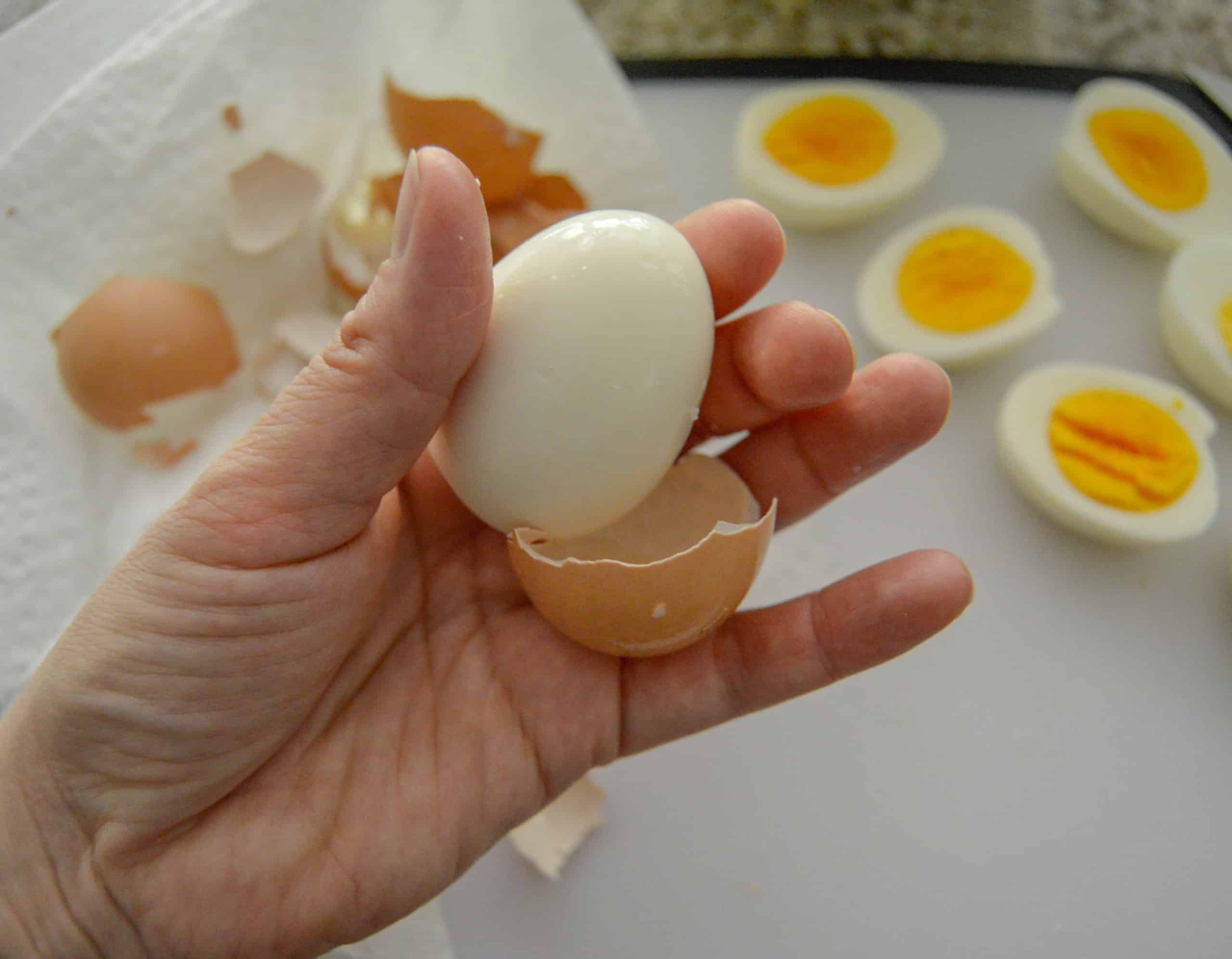 Hand holding peeled egg with hard boiled eggs cut and peeled in background