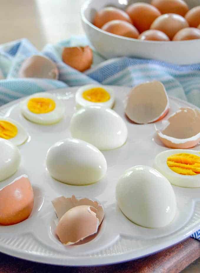 Fresh Hard Boiled eggs with raw eggs in background peeled eggs on plate with eggs cut in half next to peels