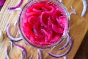 Quick pickled Red Onions with raw red onion and tongs