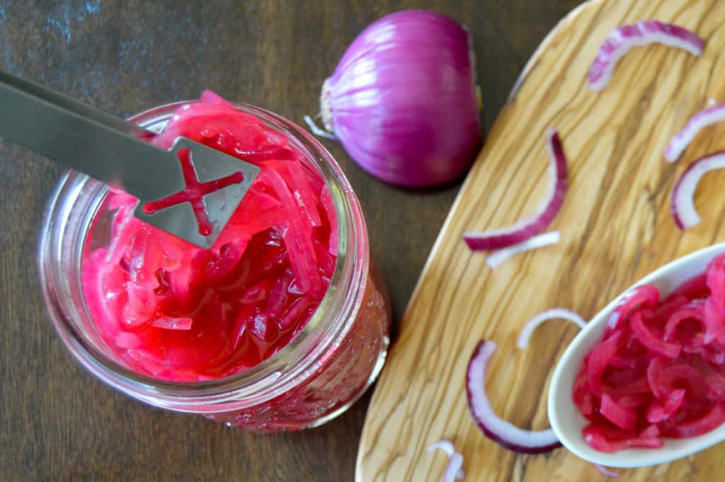 Pickled onion in jar with tongs and cutting board