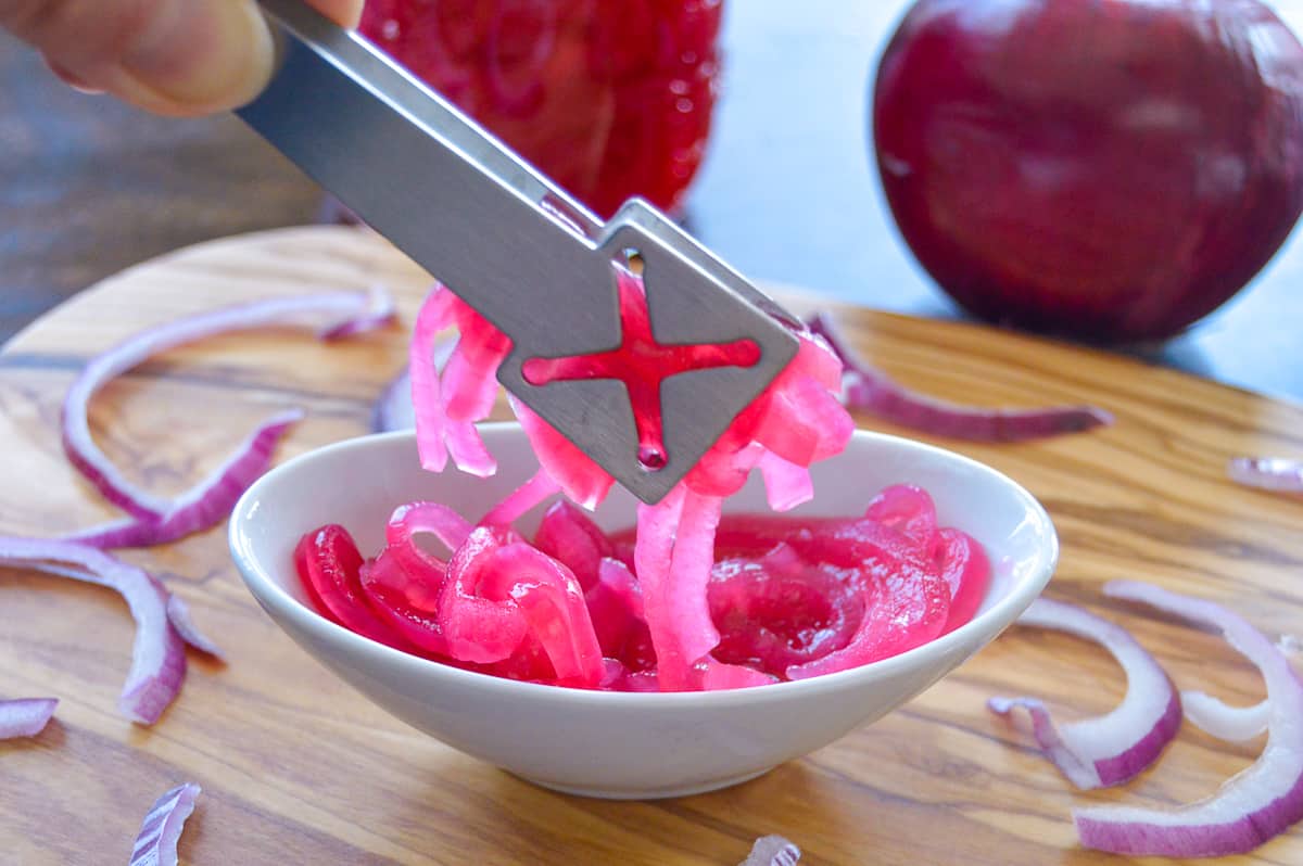 Red Onions pickled and held up with tongs