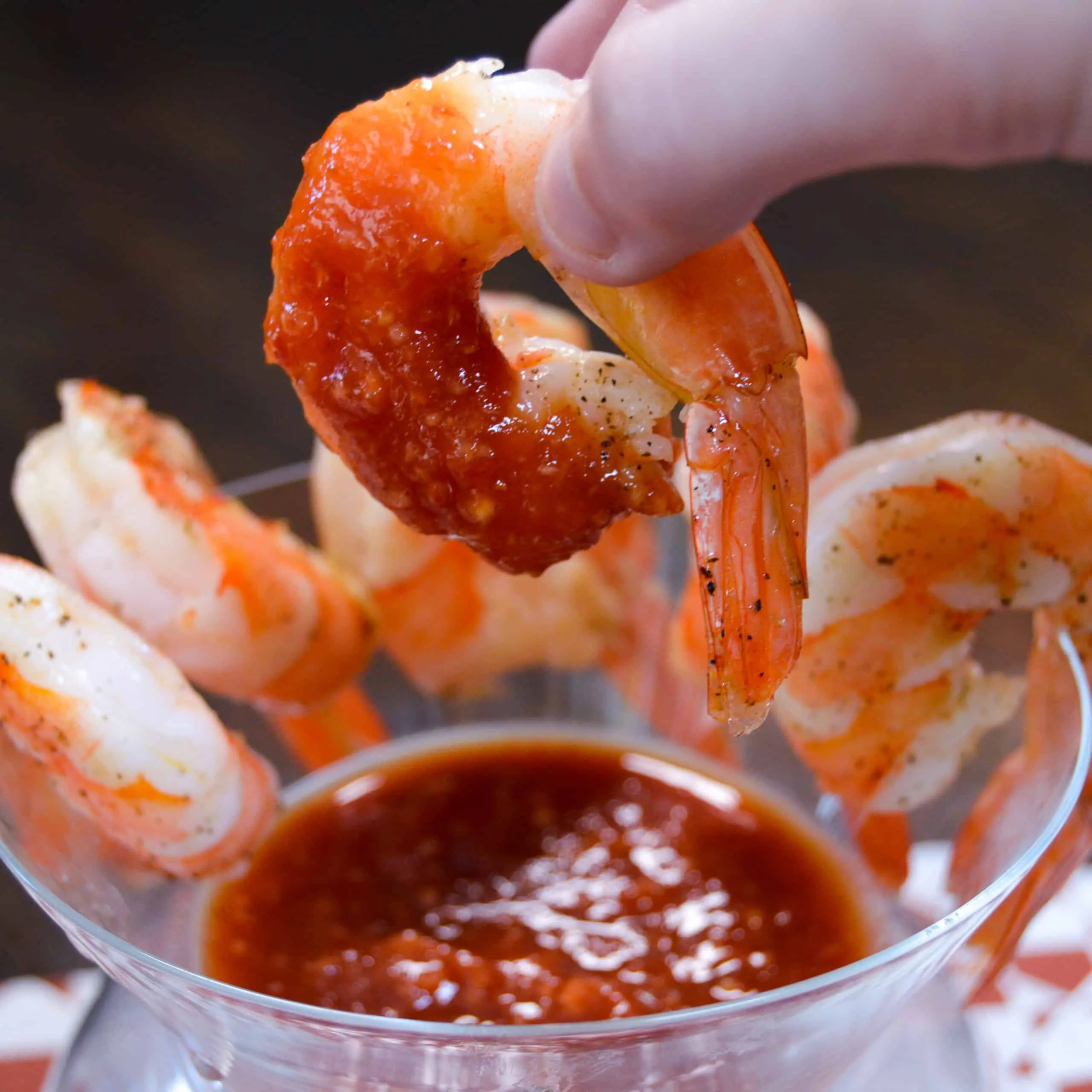 Up close shot of shrimp dipped in cocktail sauce above a glass of cocktail shrimp