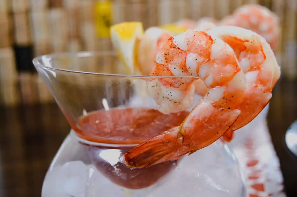 Up close shot of of shrimp hanging off glass with cocktail sauce and lemon in background