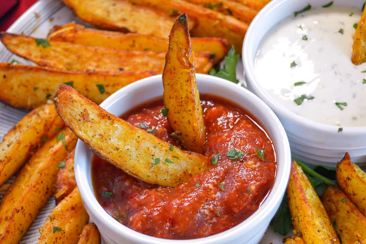 Up Close shot of Potato Wedges in ramekin with spicy ketchup and wedges in background with some ranch dip