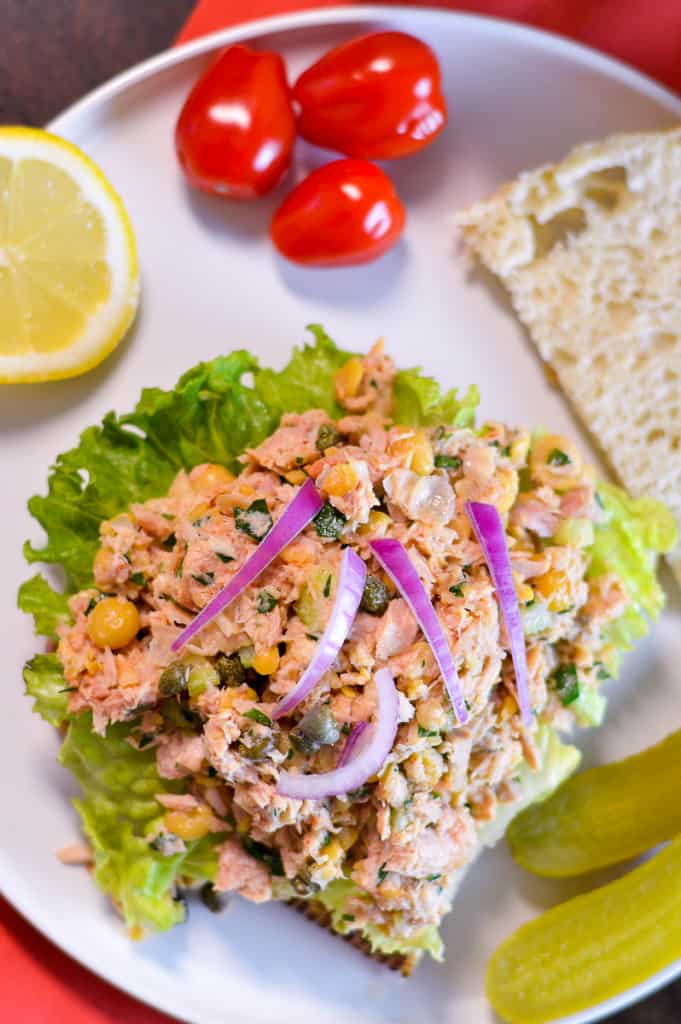 Tuna & Chickpea Salad plated over lettuce and bread, topped with some red onion with lemon wedge and some cherry tomatoes