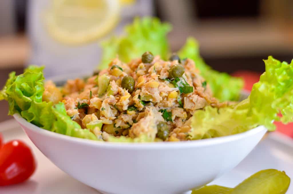 Side up close view of tuna salad with capers in bowl over top lettuce