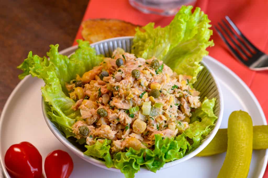 On table view of tuna chickpea salad in small bowl over lettuce with toast and glass of water