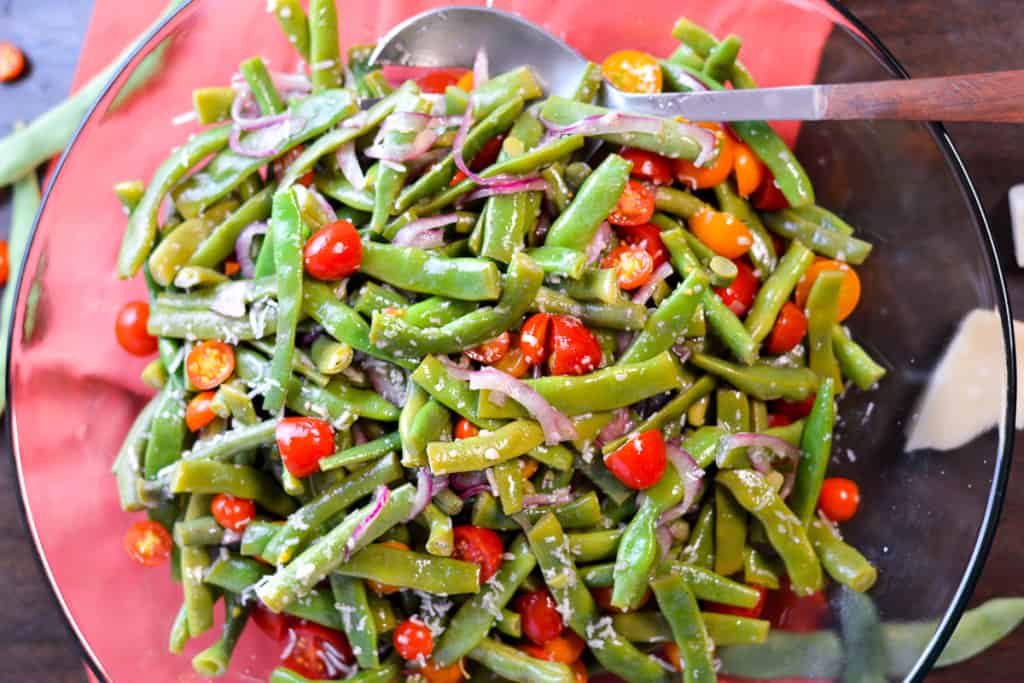 Green bean salad in a glass bowl with serving spoon in background