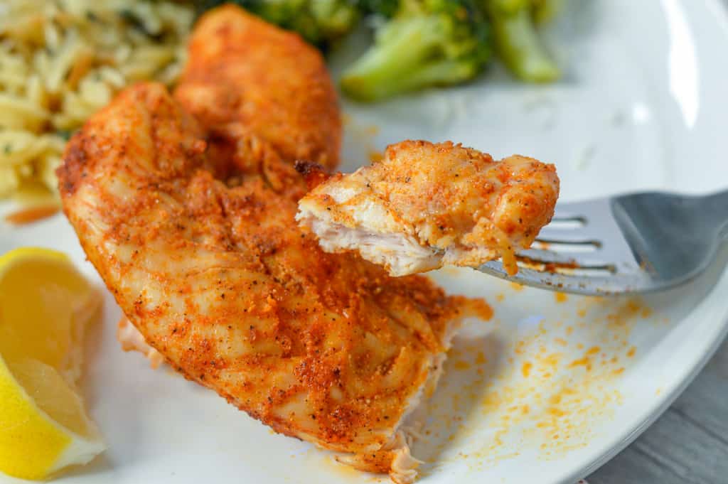 Up close look at cut off piece of chicken tender on white plate with broccoli in background