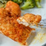 Up close look at cut off piece of chicken tender on white plate with broccoli in background