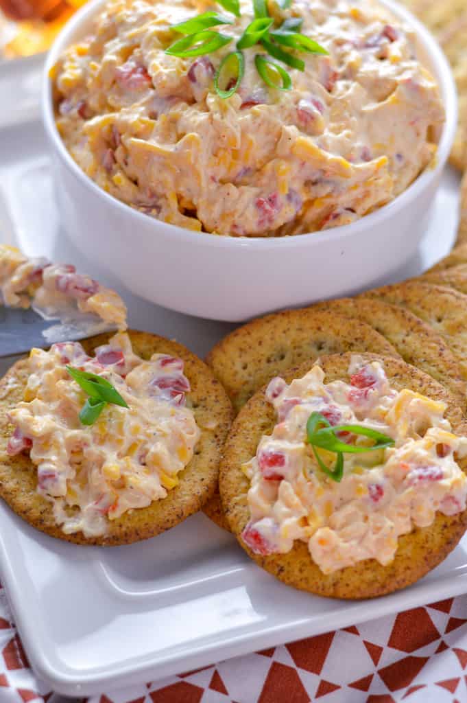 Close up view of pimento cheese spread on crackers with chopped green onion atop and knife with some spread on it