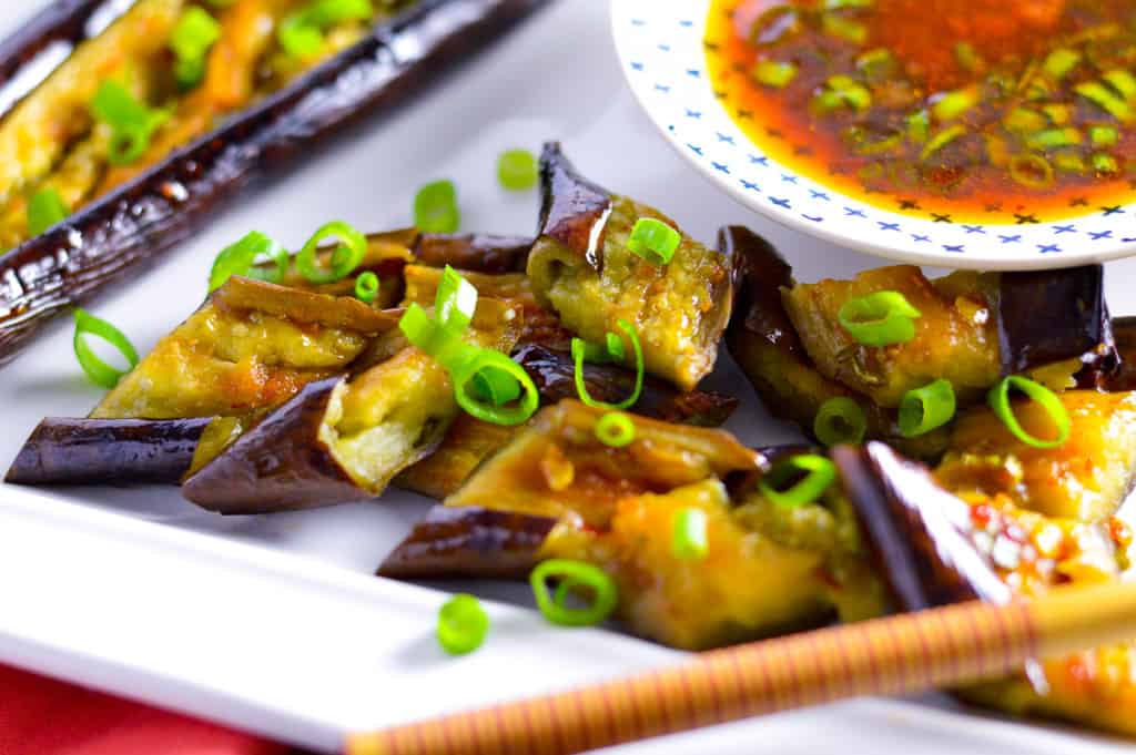 CLose up of pieces of air fried eggplant with green onions, dressing and chop sticks