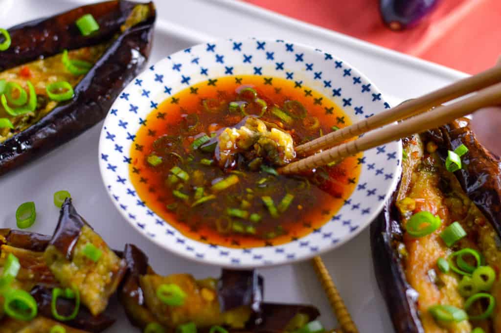 Piece of japanese eggplant being dipped in spicy Asian style spicy garlic chili dressing