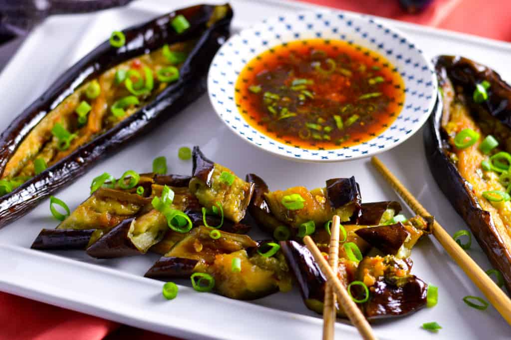 Japanese Eggplant on white platter with dressing in background, chopsticks and green onion on top