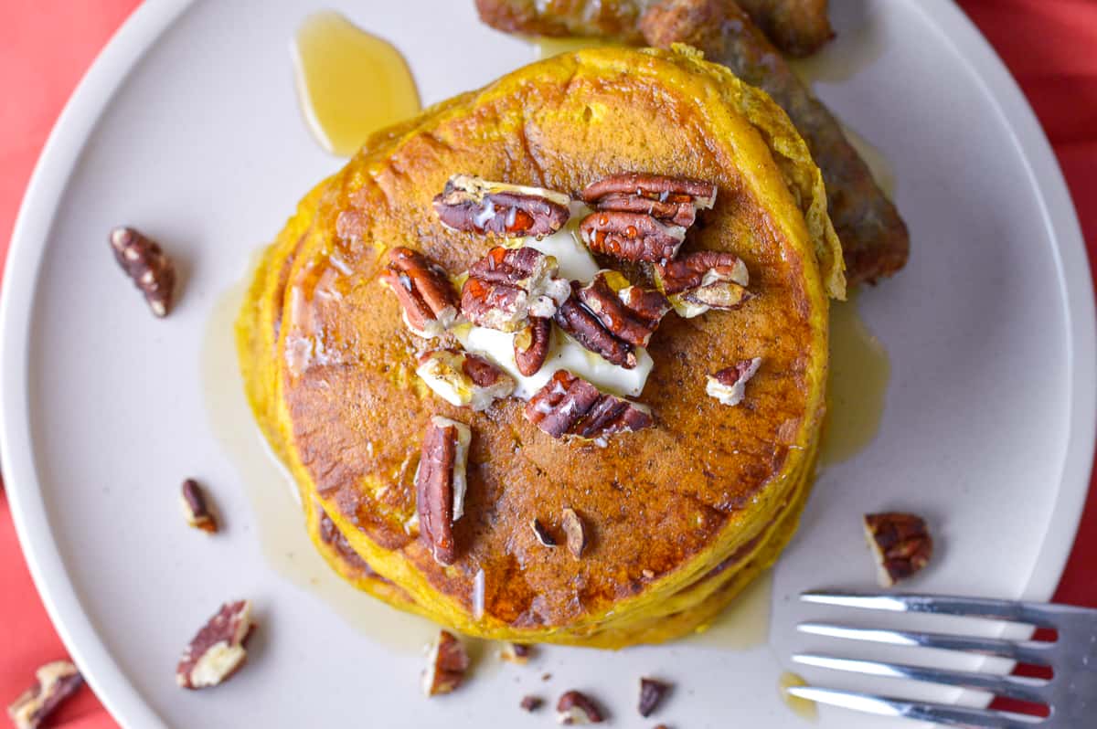 Over top view of Pumpkin Spice Pancakes with pecans, maple syrup and butter on top on white plate with sausages