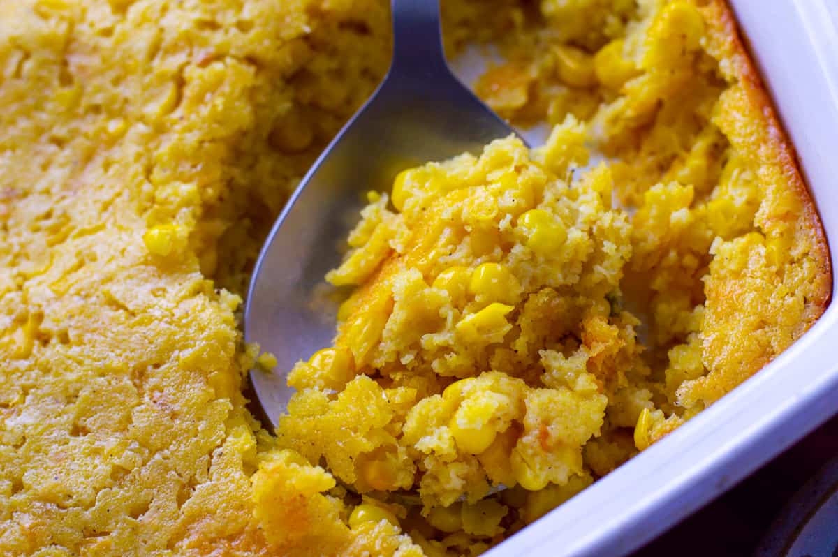 Corn Pudding Casserole on serving spoon being scooped out of baking dish, up close view