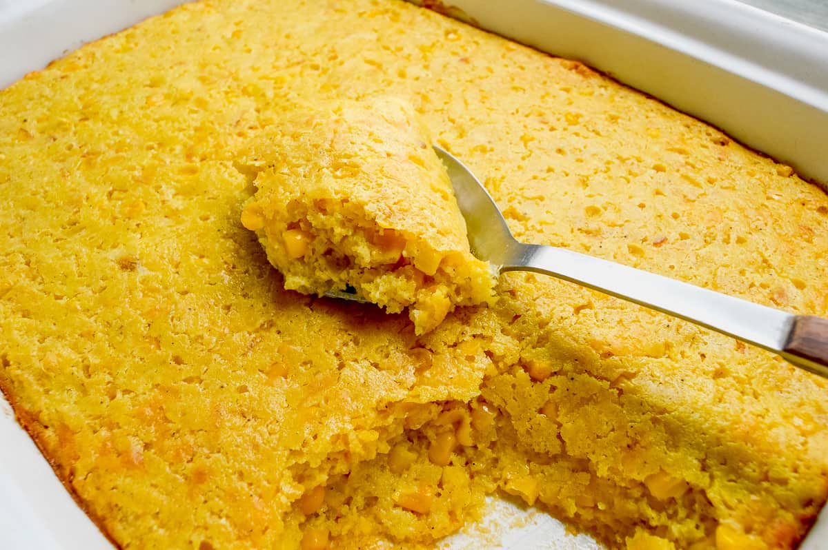 Corn Pudding Casserole in Baking dish with a spoon scooping out a bit, showing side view