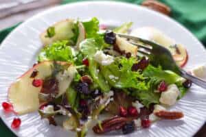 Holiday Green Salad with Apple and pomegranate on white plate with green napkin and white lights in background