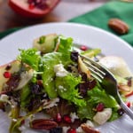 Holiday green salad with open pomegranate and white holiday lights in background