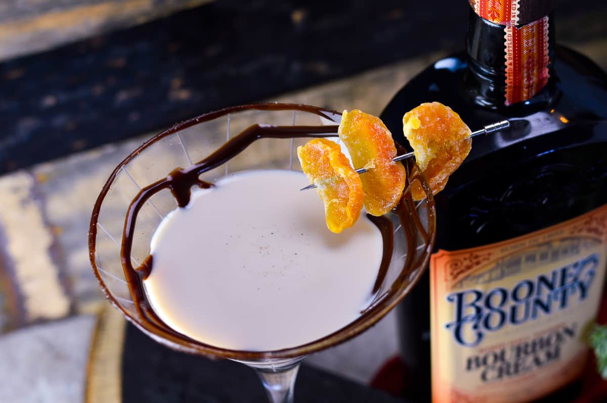 Chocolate martini with chocolate syrup and candied mandarins with bourbon cream in the background