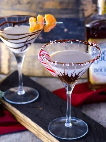 2 Bourbon Cream chocolate Martinis on bourbon stave with bourbon and barrel staves in background and some evergreen