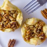 Close up of 2 pastry puffs with maple pecan pie filling on white plate with fork and pecans on the side