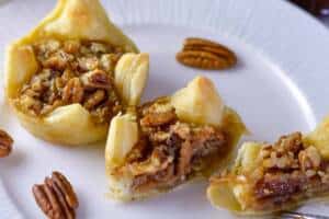 2 Maple Pecan Pie Puffs on white plate with one cut in half and a couple pecans on the side
