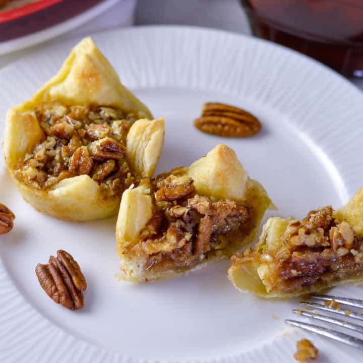 2 Maple Pecan Pie Puffs on white plate with one cut in half and a couple pecans on the side