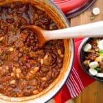 Bold Beef Chili in red dutch oven shot from above with bowl of chili on the side with toppings