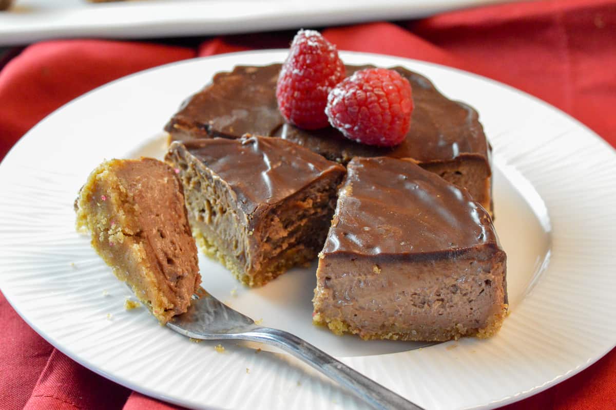 mini cheesecake cut in half with ganache on top , cut into a quarter slice and a bite on silver fork on white plate and red napkin