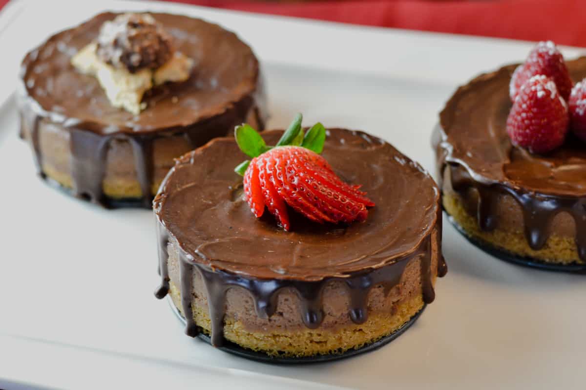 3 mini Nutella cheesecakes with different toppings: one with strawberry splayed, other with raspberries and third with ferrer rocher cut in half on graham cracker pieces on white platter