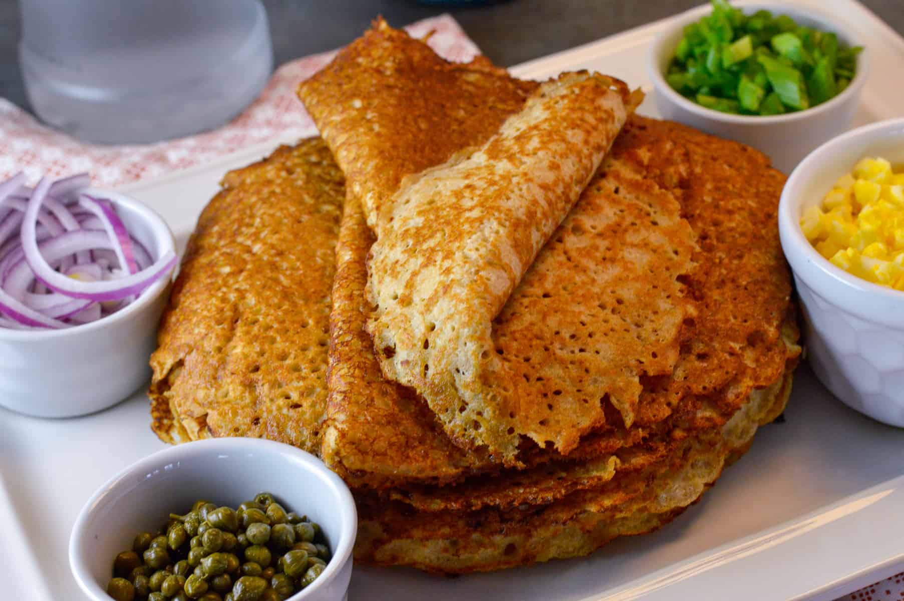 Stack of Blini with folded one on top with capers and green onion next to it