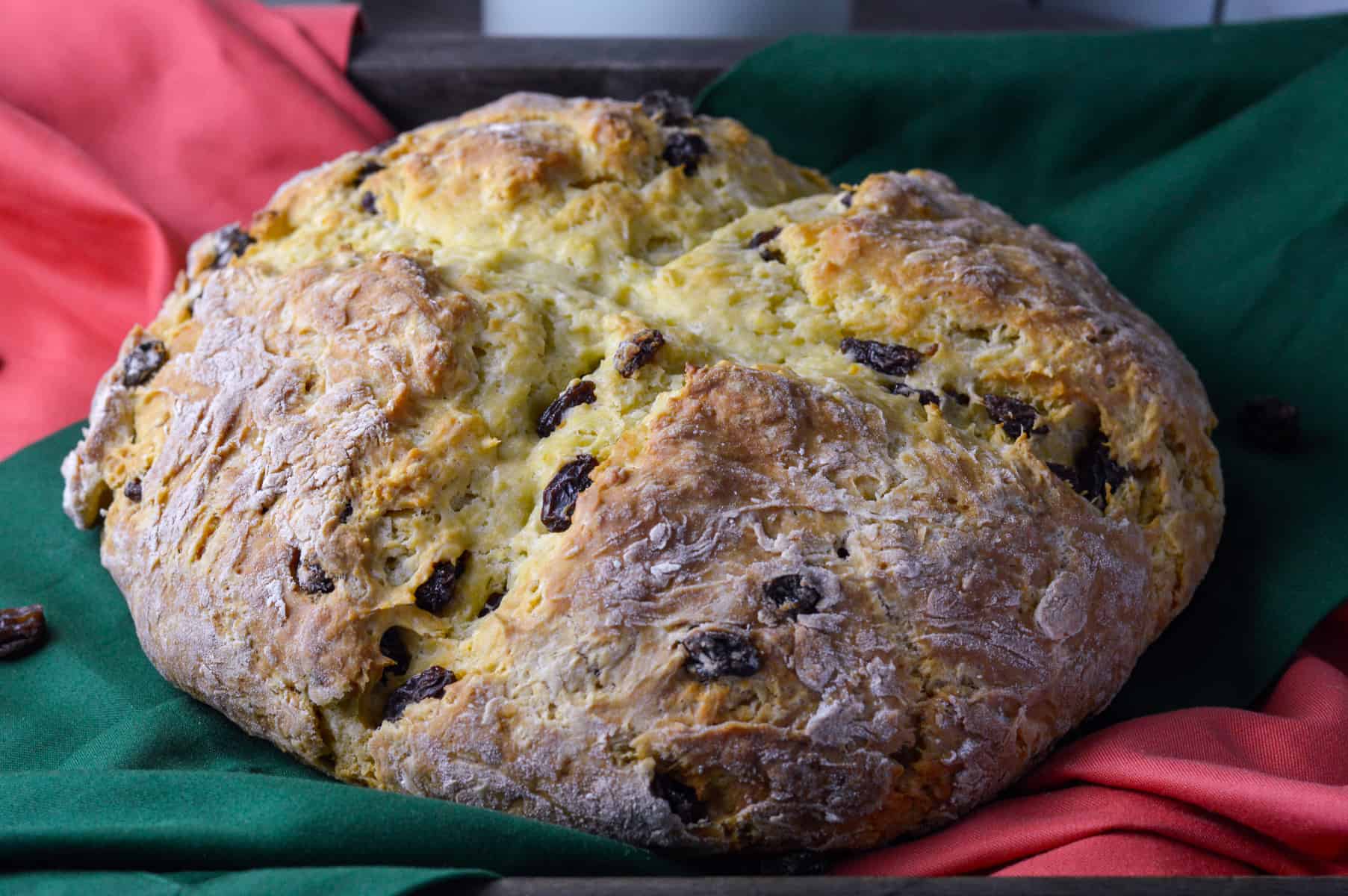 Uncut Loaf of soda bread with raisins on green and orange napkins on a serving tray with raisins scattered