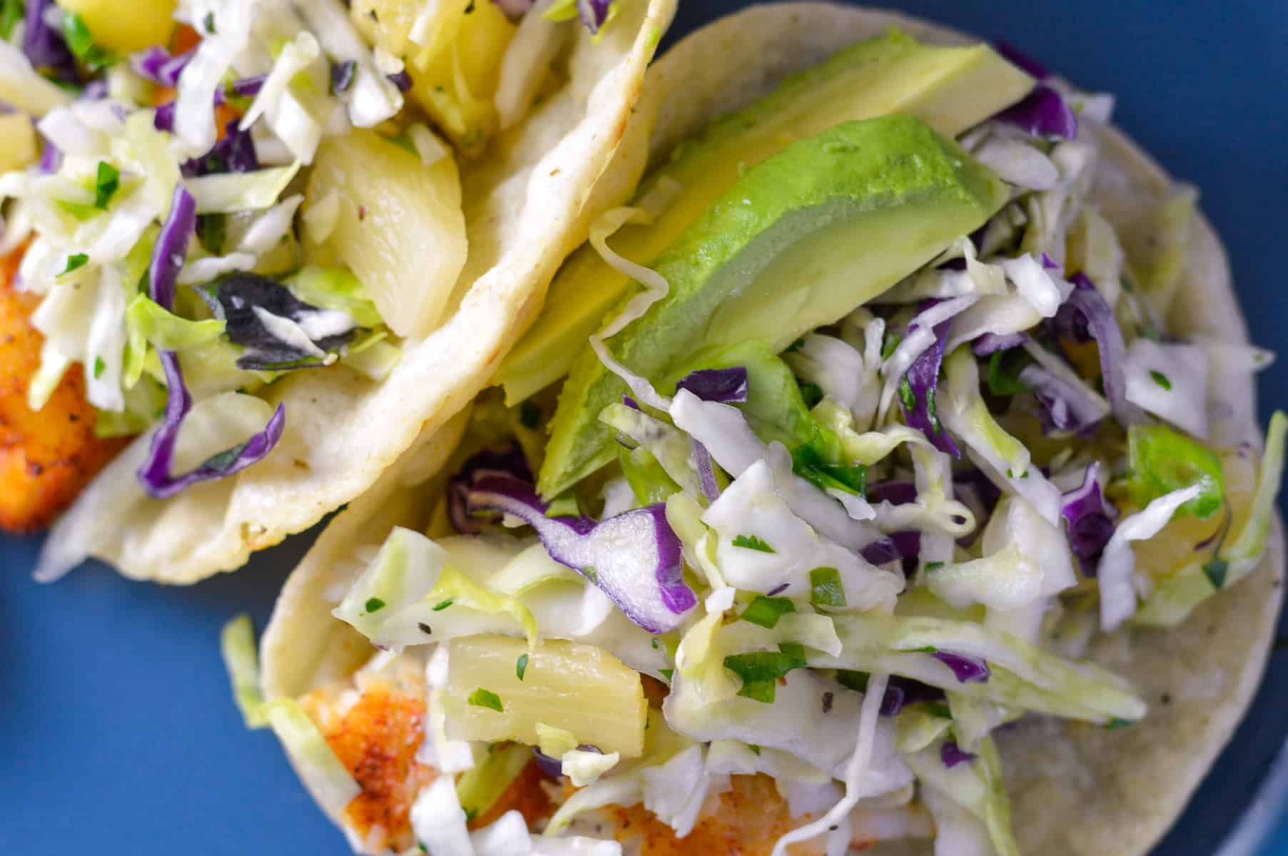 Up close shot of slaw on fish tacos with avocado on corn tortillas and plue plate